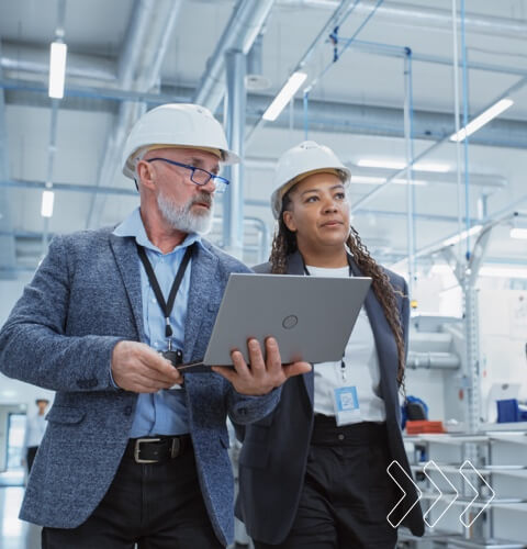 Two professional heavy industry engineers wearing hard hats at a factory, discussing safety protocols and project details